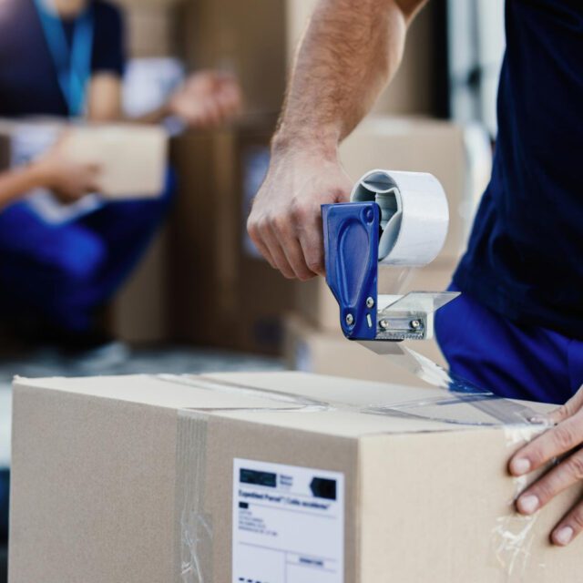 closeup delivery man closing carboard box with tape while preparing packages shipment